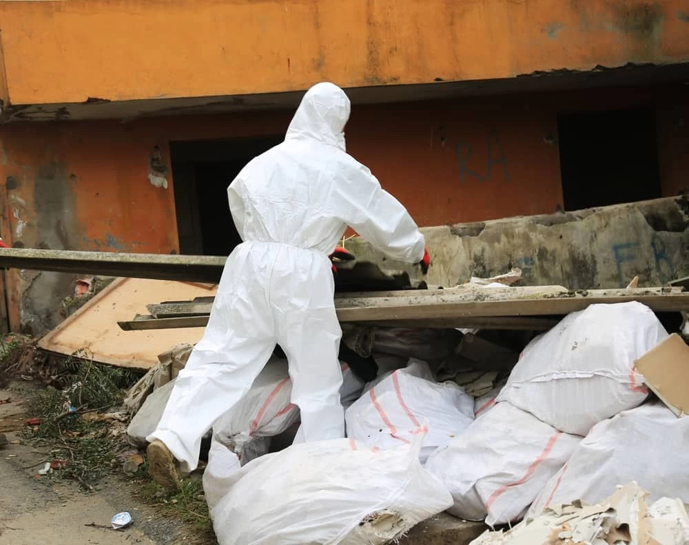 Worker wearing a white protective suit and gloves performing professional asbestos removal.
