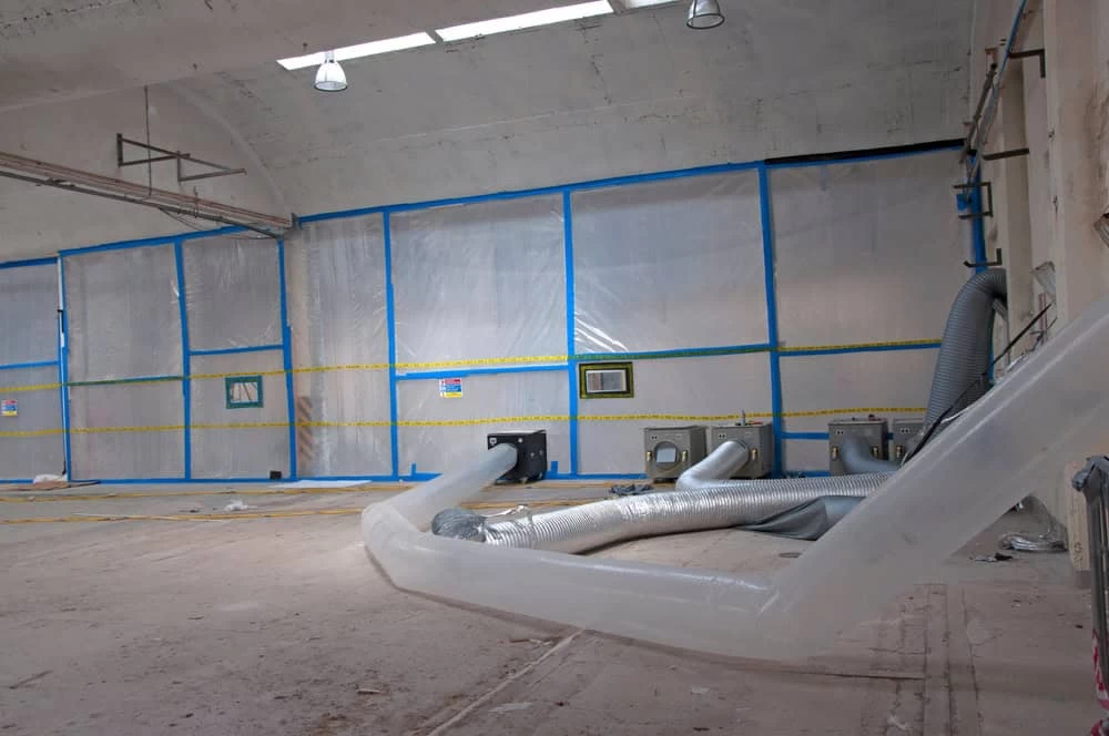 etadata Alt Text: Workers in protective suits performing asbestos removal inside a factory.