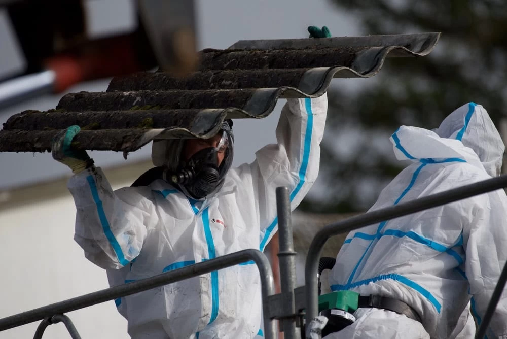 Two workers in protective suits removing asbestos from a rural school roof.