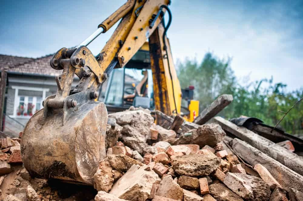 Hydraulic crusher excavator with backhoe machinery demolishing a building on-site.